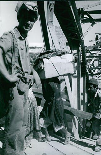 Foto vintage de oficial assistindo pessoas carregando caixas.